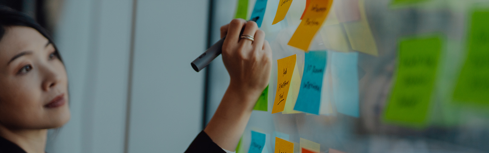 Women writing on a sticky note that is stuck on a glass panel.